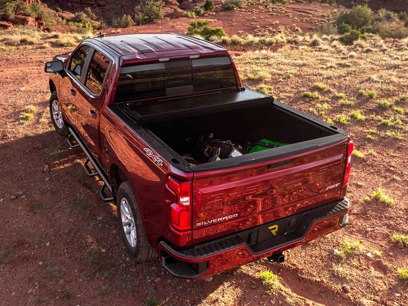 UnderCover ArmorFlex hard folding tonneau cover part-open with the rear panel folded forward over the middle panel, gear visible in the bed, high rear three-quarter view in desert scrub.