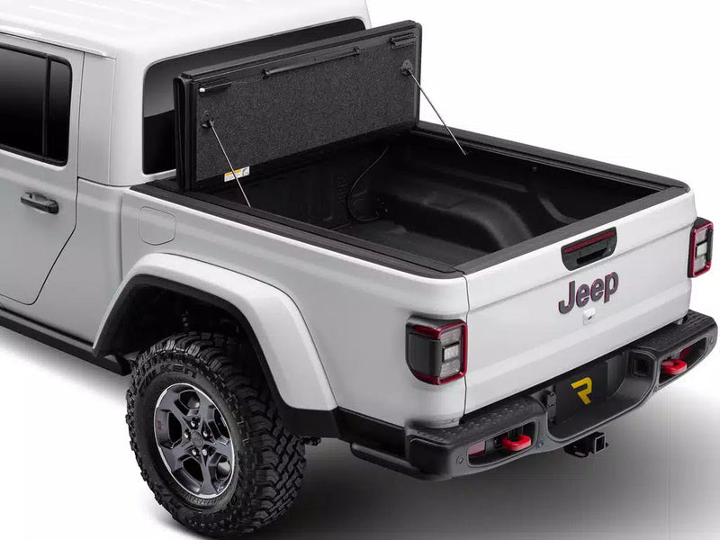 UnderCover Ultra Flex hard folding tonneau cover folded fully open and standing upright at the bulkhead, whole bed floor exposed, rear three-quarter view.