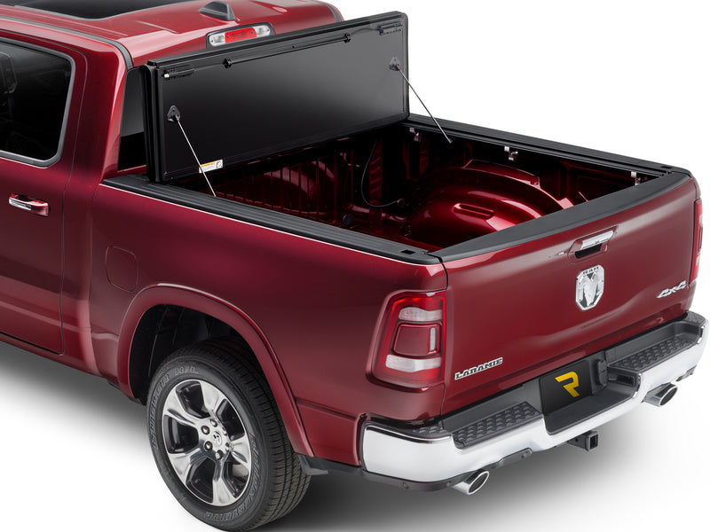 UnderCover ArmorFlex hard folding tonneau cover fully open, panels folded upright against the bulkhead on prop rods with the whole bed floor exposed, rear three-quarter view.