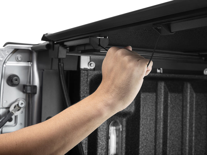 A hand reaching in at the tailgate to operate the ArmorFlex rear latch release, close-up detail.