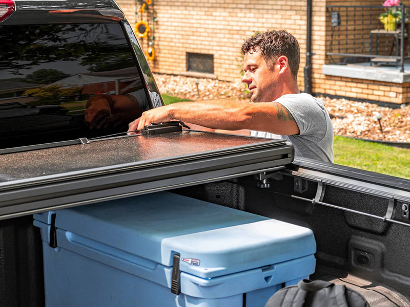 UnderCover Select folded forward while a dry bag and a cooler are loaded into the open bed on a 2019-2026 Chevrolet Silverado 1500