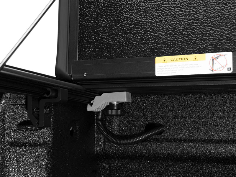Close-up of the ArmorFlex drain tube and its bed-rail fitting at the front corner of the bed, cover raised above.