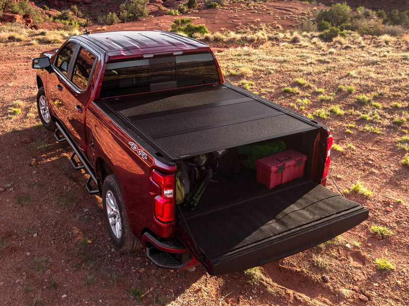 UnderCover ArmorFlex hard folding tonneau cover with the rear section open and the tailgate down, gear loaded in the bed, high rear three-quarter view in desert scrub at golden hour.