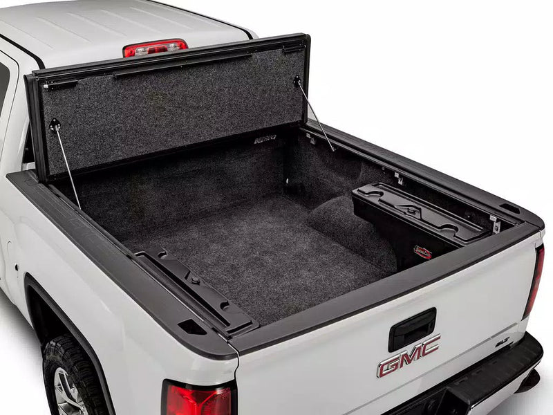UnderCover Ultra Flex hard folding tonneau cover folded fully open and propped upright at the bulkhead, full bed floor exposed, rear three-quarter view.