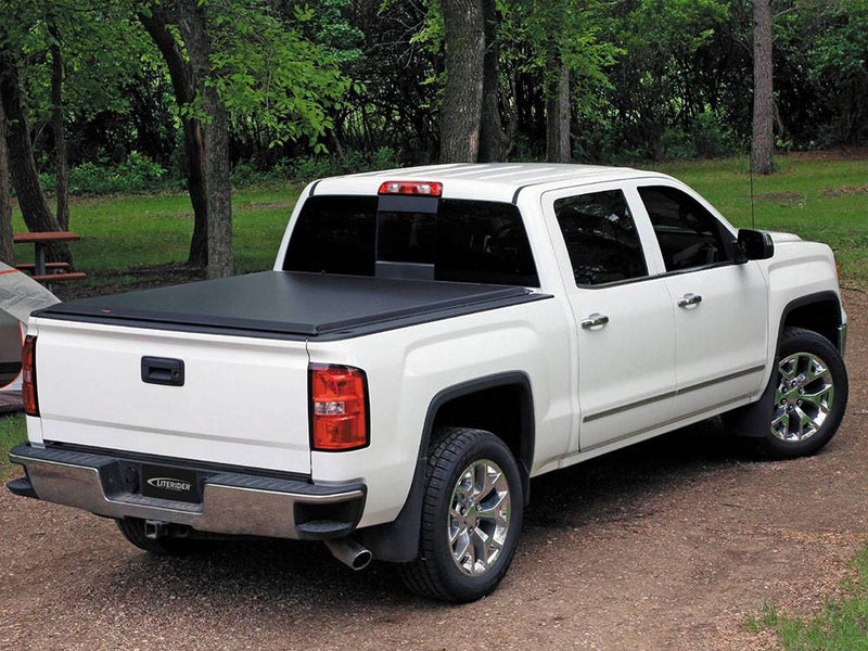 White crew cab pickup at a wooded campsite with a black roll-up tonneau cover closed over the bed