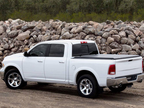 White pickup on dirt in front of a rock pile, black roll-up tonneau cover closed over the bed