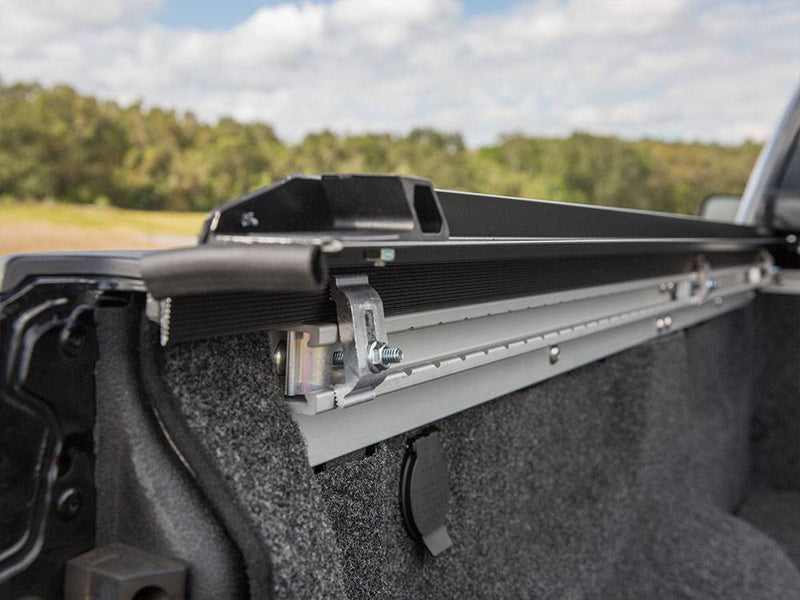 Aluminum side rail and clamp inside a carpet-lined bed, cover rolled toward the cab