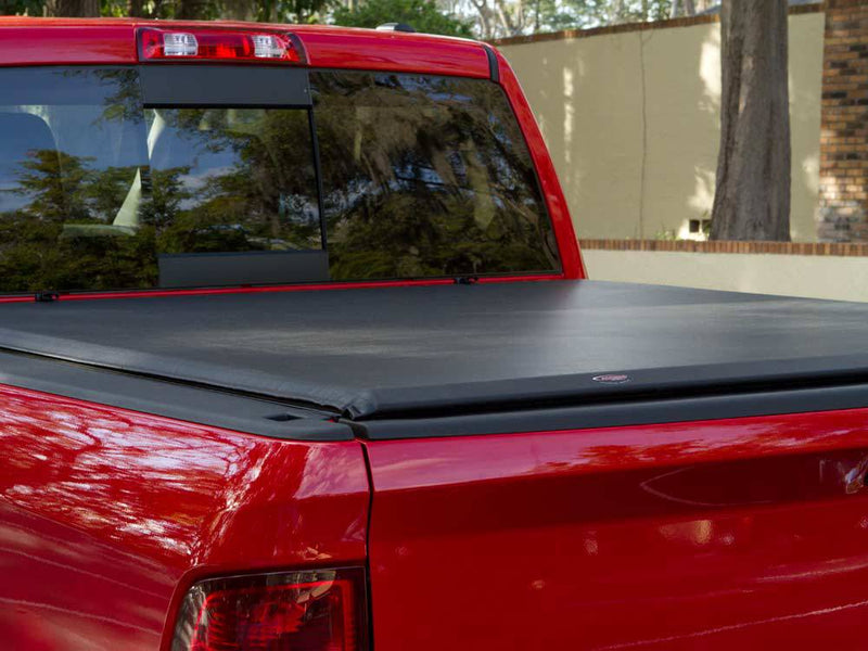Close view of a black roll-up tonneau cover closed flush over a red pickup bed, rear corner and cab window in frame