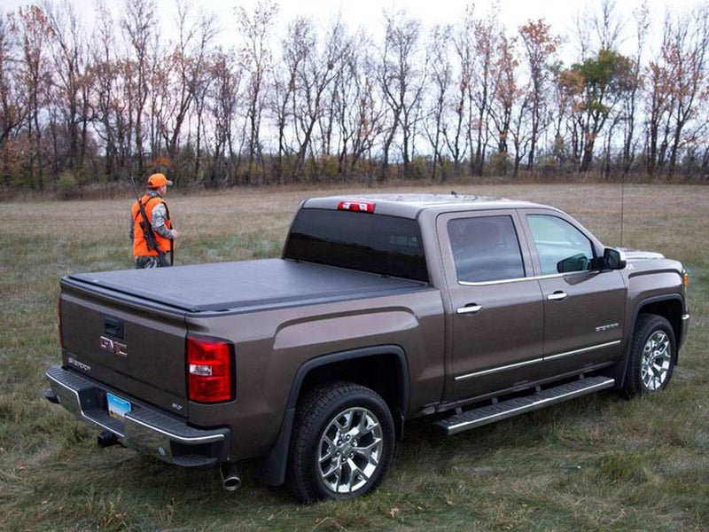 Roll-up tonneau cover closed over the bed of a brown pickup in a field, man in orange walking behind