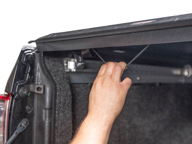 Hand pulling the latch release cord under the rear edge of the closed cover, tailgate open