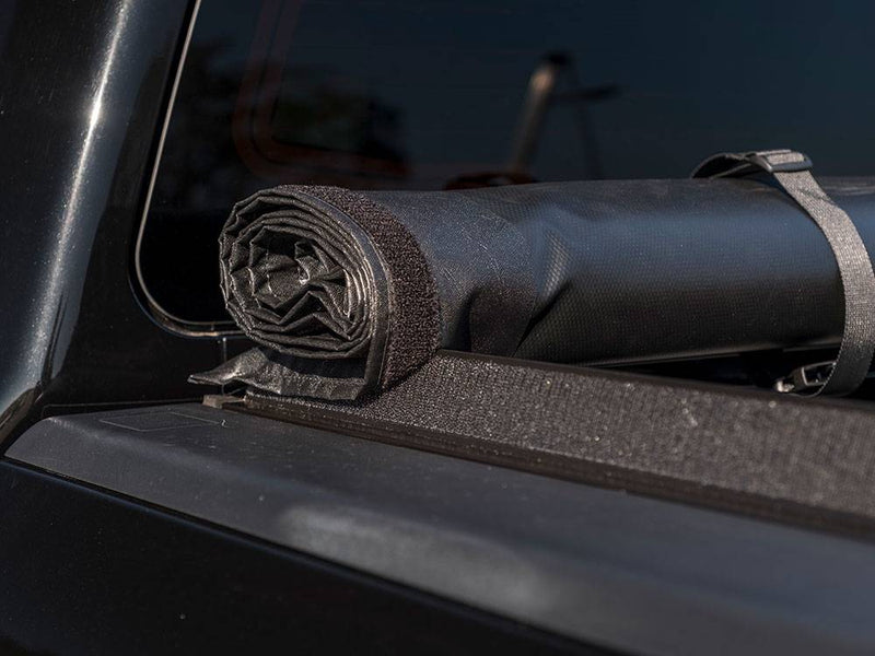 Rolled vinyl cover held against the cab by a nylon storage strap on the hook-and-loop side rail