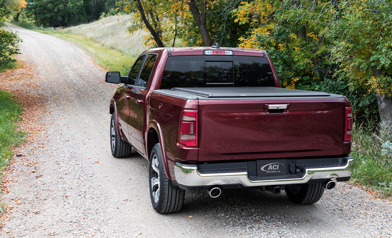 Access Original roll-up tonneau cover on a pickup bed: maroon pickup on a gravel lane with a black roll-up cover closed flat over the bed, rear view