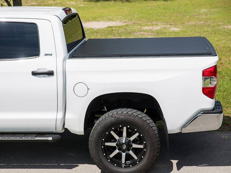Side view of a white pickup with a black soft roll-up cover closed level with the bed rails