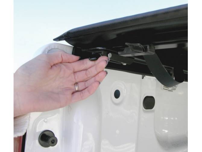 Hand reaching under the raised rear rail to the latch and tension strap