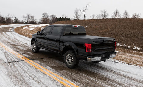 Access Vanish roll-up tonneau cover on a pickup bed: black crew cab pickup on a snowy road, black low-profile roll-up cover closed over the bed