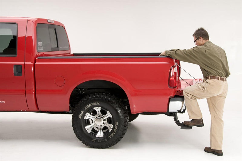 A man stands on the BedStep to reach over the bed side of a red heavy-duty pickup, studio background