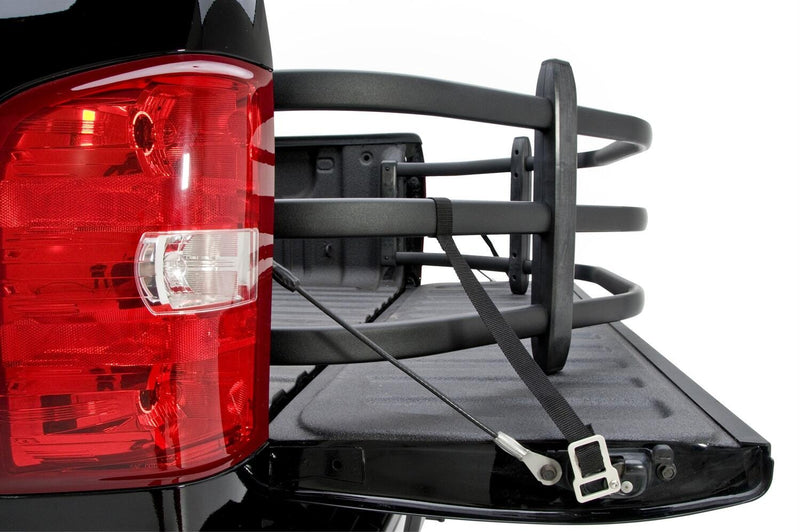 Black bed extender strapped across a lowered tailgate beside a red tail lamp