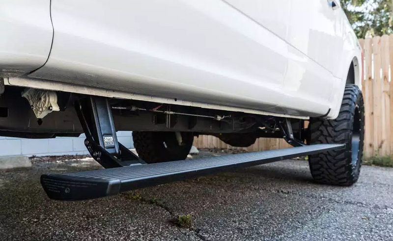 PowerStep deployed under the doors of a lifted white pickup on asphalt, low angle