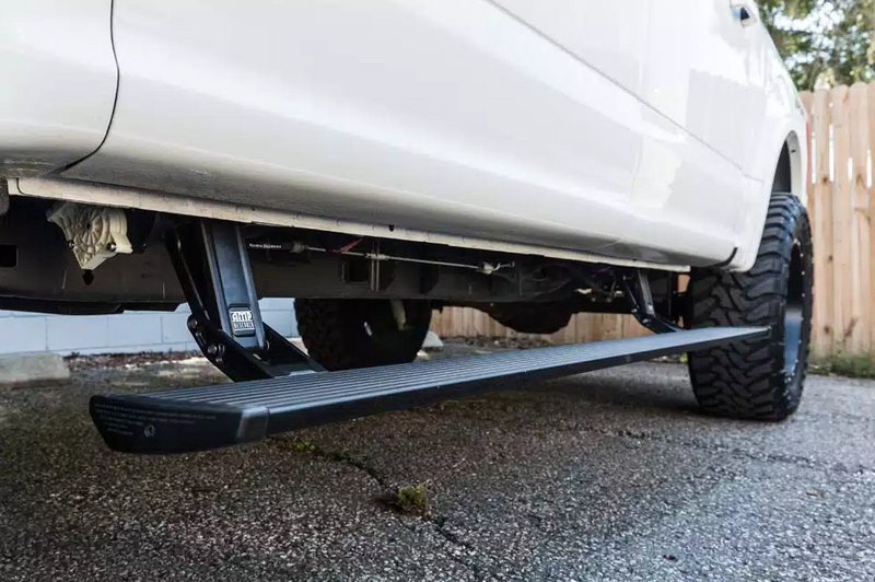 PowerStep deployed under the doors of a lifted white pickup on asphalt, low angle