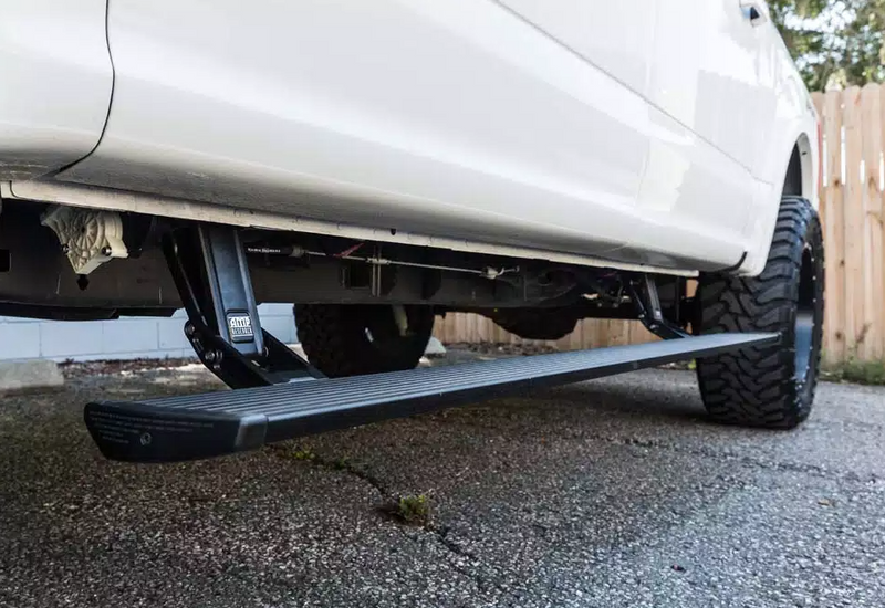 PowerStep deployed under the doors of a lifted white pickup on asphalt, low angle