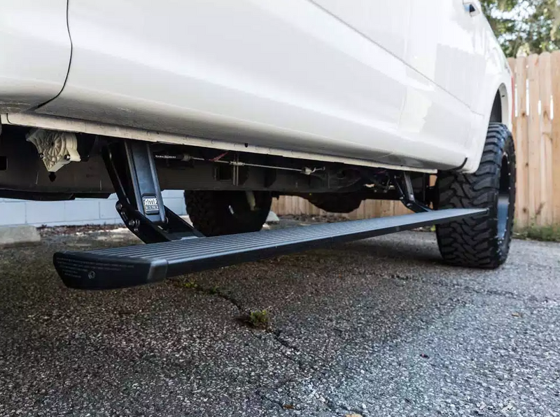 PowerStep deployed under the doors of a lifted white pickup on asphalt