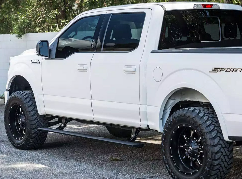 Lifted white crew-cab pickup with the PowerStep deployed, three-quarter side view on asphalt, second angle