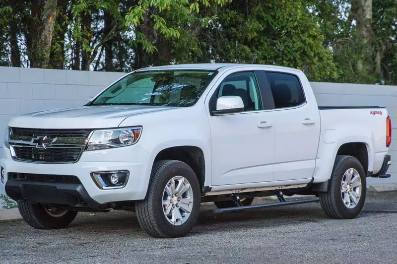 White mid-size crew-cab pickup parked on asphalt, running board under the doors, second angle