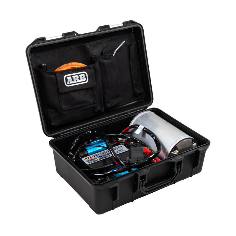 ARB CKMTP12 portable twin motor 12V air compressor shown in its open black hard case with the twin motor unit, a polished cylindrical air tank, coiled battery leads and an orange air hose in the ARB branded lid pocket