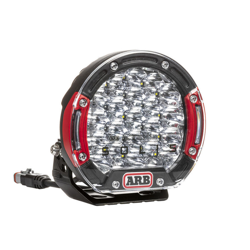 ARB Intensity SOLIS LED driving light with red bezel inserts and mounting bracket, front three-quarter view on white