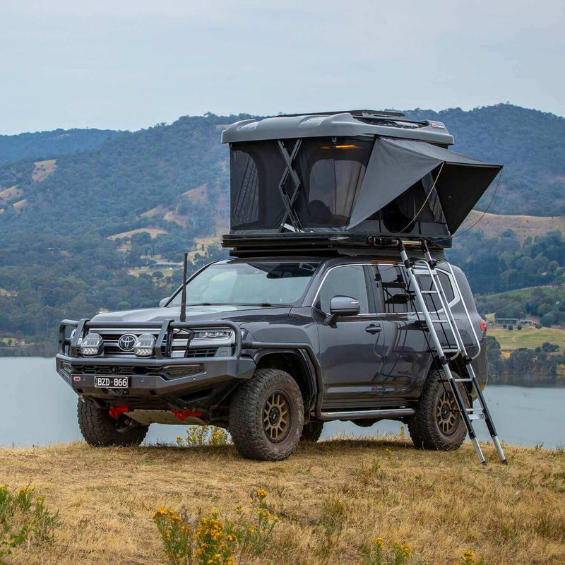 ARB Altitude hardshell rooftop tent raised on a roof rack with lake and hills behind