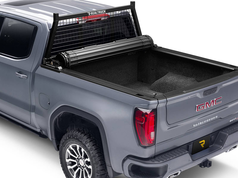 BackRack Safety: gray GMC Sierra with a black Safety headache rack and a rolled-up hard tonneau cover at the front of a carpeted bed