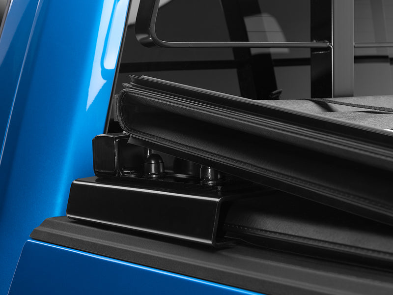 BackRack Tonneau Adapter: black tonneau adapter bracket on the bed rail of a blue truck beside a folded tonneau cover