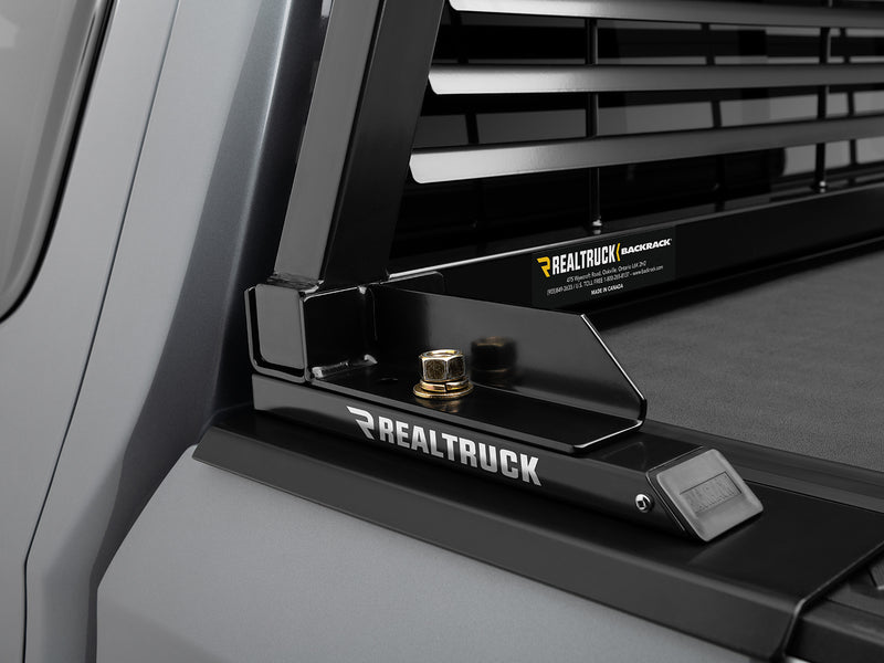 BackRack Tonneau Adapter: black tonneau adapter bracket with RealTruck lettering holding a louvered rack upright above a gray truck bed rail