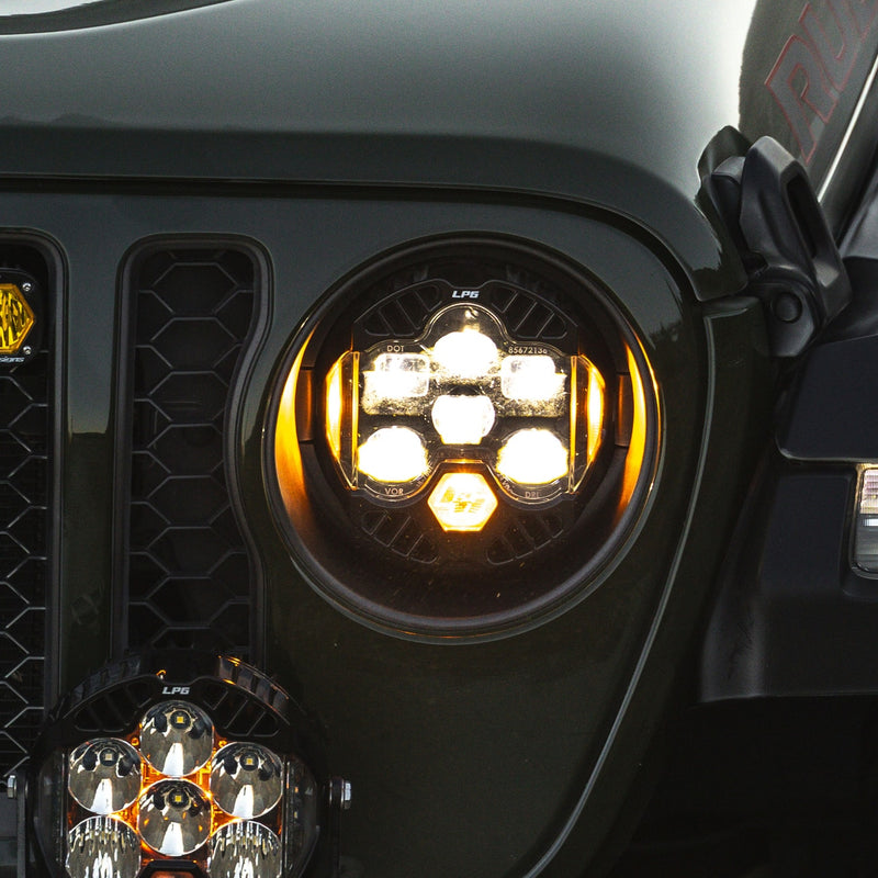 Baja Designs DOT LP6 LED Headlight Replacement Pair on a Jeep Wrangler: an LP6 LED headlight glowing in the fender of a green Jeep Wrangler beside the slotted grille, with an auxiliary pod below