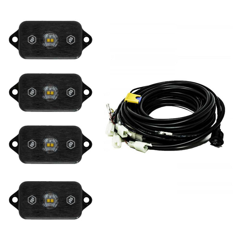 Baja Designs LED Rock Light Kit, complete kit on a studio background: four black LED rock light pods with white-and-amber centers shown with a coiled multi-lead wiring harness on white