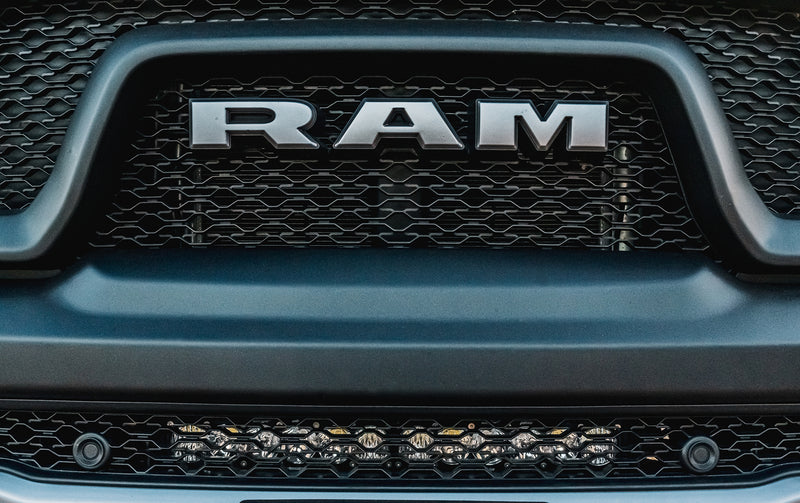 Baja Designs OnX6+ 20" Bumper Light Bar Kit on a Ram 1500: A light bar mounted in the lower grille opening of a gray Ram below the grille lettering