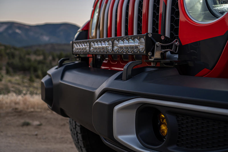 Baja Designs OnX6+ 30" Bumper Light Kit on a Jeep Wrangler JL: close view of a red Jeep front bumper with a 30" OnX6+ light bar across the top and an amber fog pod, with hills behind