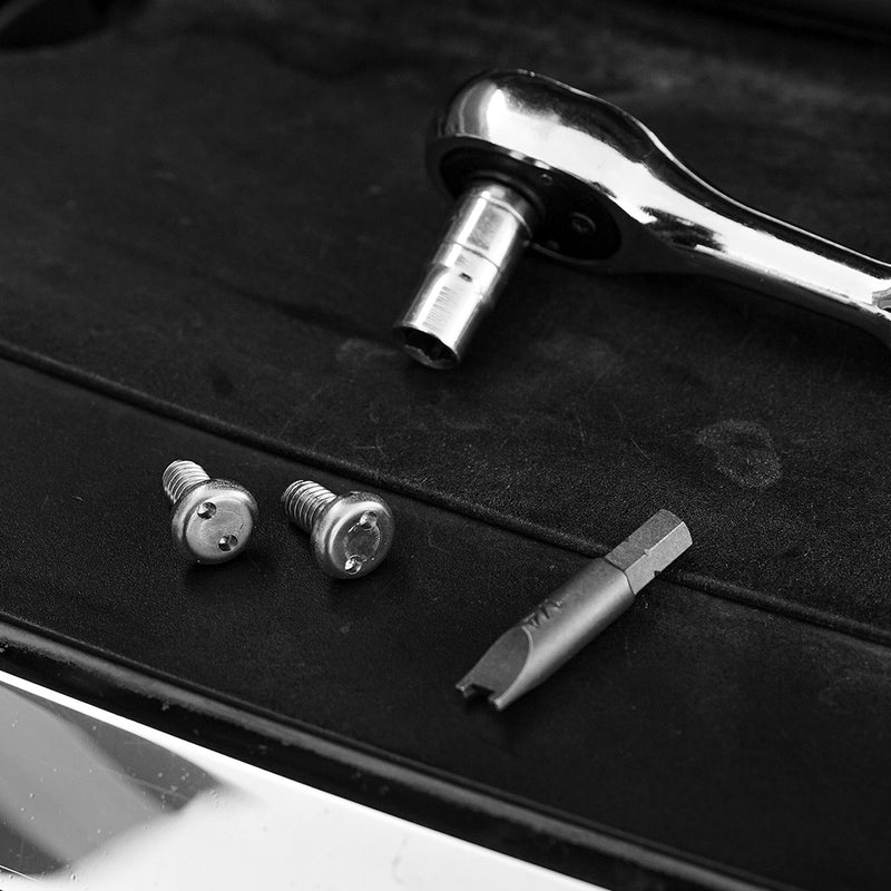Close-up of the Baja Designs OnX6+/S8/XL/LP Series Security Hardware Kit: two tamperproof security screws and a matching driver bit beside a ratchet on a black light housing