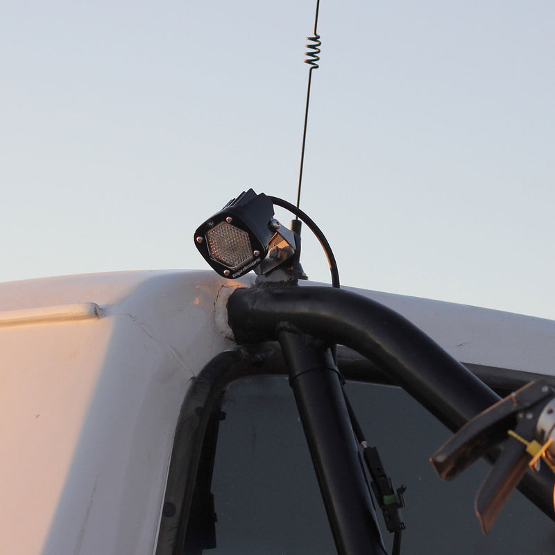 Baja Designs S1 Black LED Auxiliary Light Pod Pair on a vehicle: A black S1 light pod mounted on a tube at the roof edge of a vehicle against a pale sky