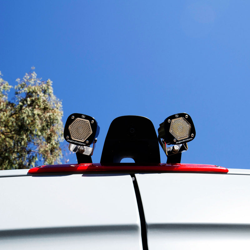 Baja Designs S1 Dual Reverse Light Kit on a vehicle: close view of two S1 pods on a bracket above a van's third brake light against a blue sky