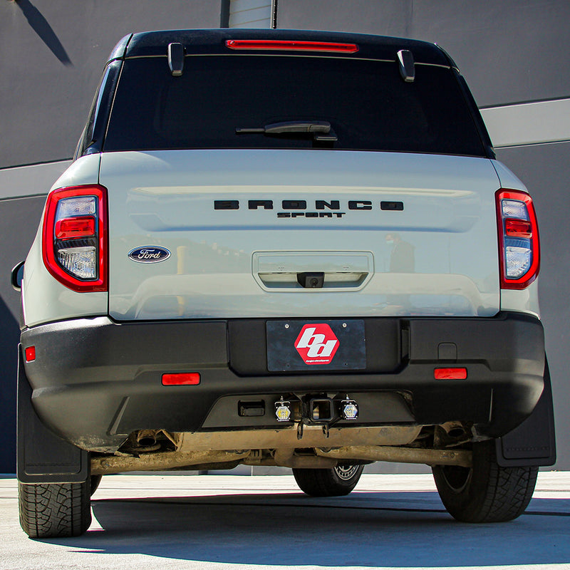 Baja Designs S1 Dual Reverse Light Kit installed on a Ford Bronco Sport: rear view of a white Ford Bronco Sport with a Baja Designs logo plate and reverse lights under the bumper