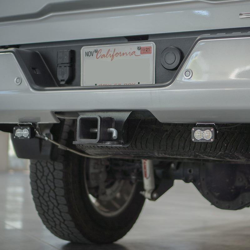 Baja Designs S2 Sport Dual Reverse Light Kit on a vehicle: two S2 Sport pods mounted under the rear bumper of a silver pickup on either side of the receiver hitch