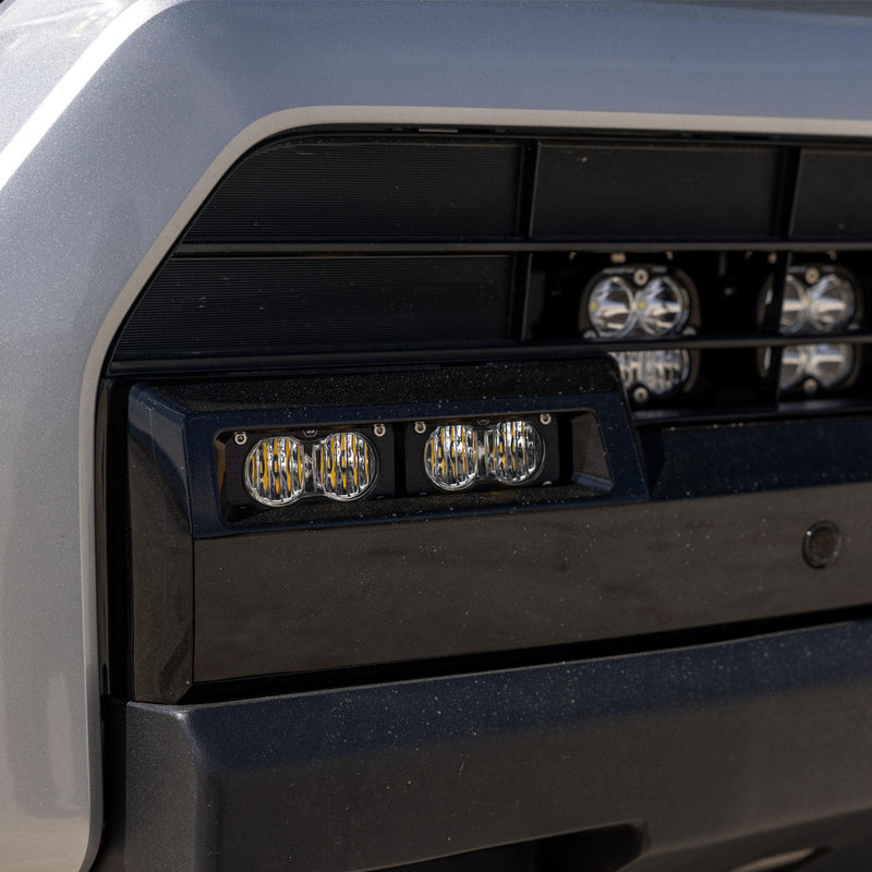 Baja Designs S2 Sport OEM Fog Light Replacement Kit on a vehicle: close view of two clear S2 fog lights set into a black lower bumper opening on a silver vehicle