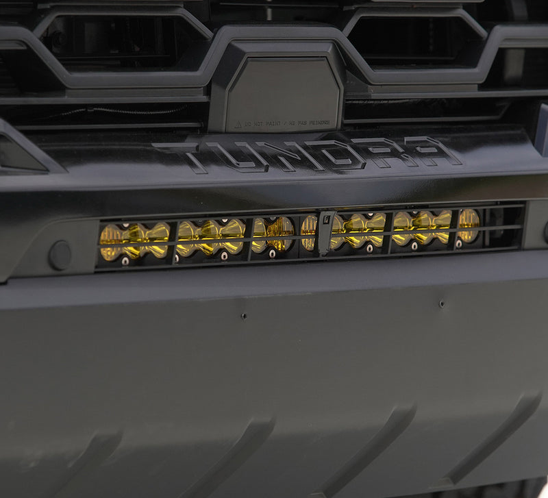 Baja Designs S8 20" Behind Bumper Light Bar Kit on a Toyota Tundra: an amber-lens light bar mounted behind the front bumper of a black Toyota Tundra below the grille lettering