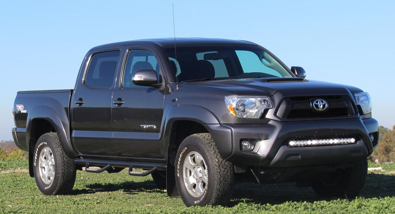 Baja Designs S8 30" Bumper Light Kit installed on a Toyota Tacoma: A black double-cab Toyota Tacoma parked on grass with a light bar mounted in the lower front bumper