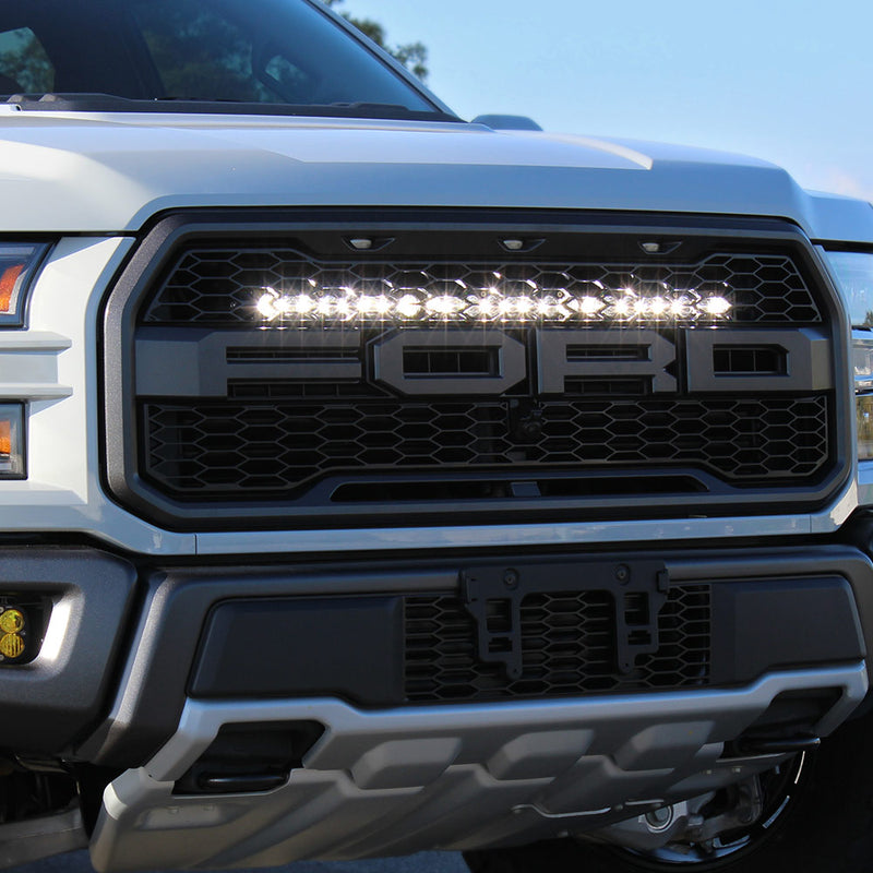 Baja Designs S8 30" Grille Upper Light Bar Kit on a Ford F-150 Raptor: front view of a white Ford Raptor with a lit light bar across the top of the grille above the FORD lettering