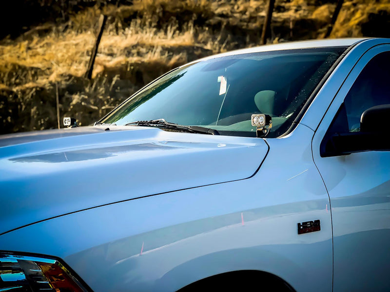 Baja Designs Squadron Pro A-Pillar Light Kit installed on a Ram 1500 Classic: A light blue Ram pickup with a Squadron LED pod mounted at the driver side A-pillar