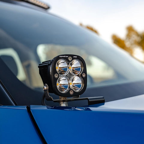 Baja Designs Squadron Pro A-Pillar Light Kit on a vehicle: A Squadron Pro LED pod with a clear lens on an A-pillar bracket at the base of a blue vehicle's windshield