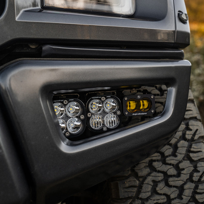 Baja Designs Squadron/S2 SAE Pro Fog Pocket Light Kit on a vehicle: close view of a dark bumper fog pocket fitted with two clear Squadron pods and an amber S2 pod