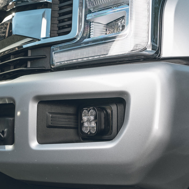 Baja Designs Squadron Sport Fog Pocket Light Kit on a Ford: close view of a clear Squadron pod seated in the fog pocket of a silver Ford bumper